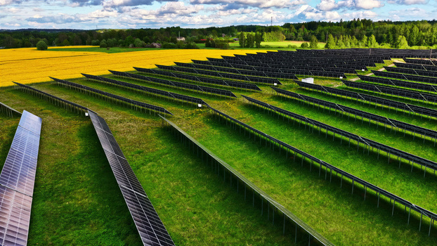 Aerial view of rows of solar panels installed in a green field next to a vibrant yellow rapeseed field under a cloudy sky in Latvia. Aerial view of rows of solar panels installed in a green field next to a vibrant yellow rapeseed field under a cloudy sky in Latvia.