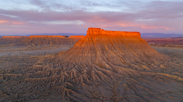 Aerial view of the dramatic Factory Butte mesa rising from the eroded badlands landscape under a soft sunset sky in Hanksville Utah United States.