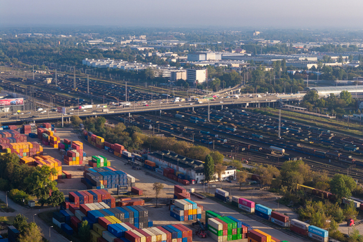 Warsaw Poland 14 September 2026 Aerial view of a large shipping hub with colorful freight containers extensive railway tracks and a busy highway overpass under a clear sky.