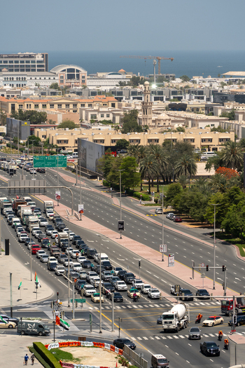 Aerial view of heavy traffic on a multi lane highway surrounded by urban buildings palm trees and a mosque minaret with the sea on the horizon in Dubai Dubai United Arab Emirates. Aerial view of heavy traffic on a multi lane highway surrounded by urban buildings palm trees and a mosque minaret with the sea on the horizon in Dubai Dubai United Arab Emirates.