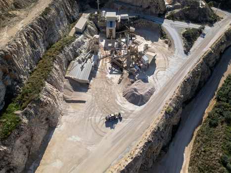 Aerial view of a stone quarry with industrial crushing machinery piles of gravel and a vehicle on a dirt road surrounded by rocky cliffs in Teulada Valencian Community Spain.