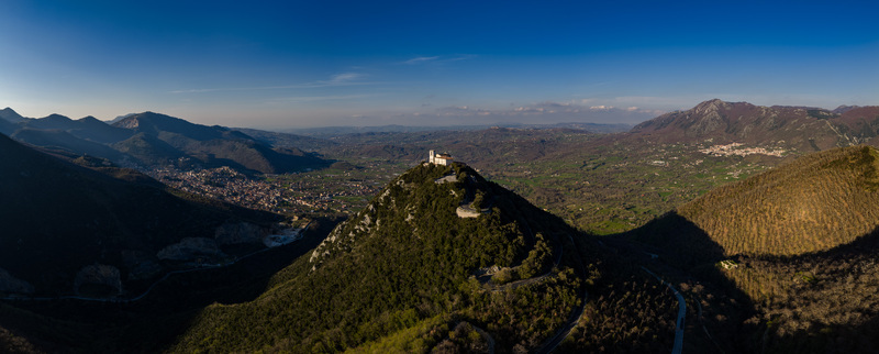 Aerial view of Santuario del Santissimo Salvatore on a mountain peak overlooking the valley and town under a clear blue sky Montella Campania Italy. Aerial view of Santuario del Santissimo Salvatore on a mountain peak overlooking the valley and town under a clear blue sky Montella Campania Italy.
