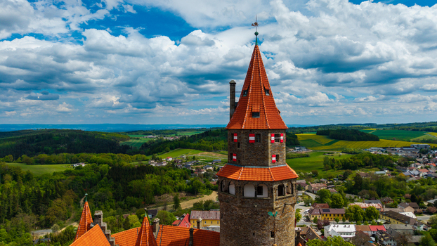 Aerial view of Bouzov Castle featuring its iconic stone tower with red tiled roofs overlooking the rolling green hills and village of Bouzov Olomoucky kraj Czechia. Aerial view of Bouzov Castle featuring its iconic stone tower with red tiled roofs overlooking the rolling green hills and village of Bouzov Olomoucky kraj Czechia.