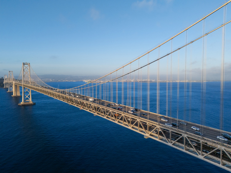 Aerial view of the San Francisco Oakland Bay Bridge with traffic flowing across the suspension structure over the blue waters of the bay in San Francisco California United States. Aerial view of the San Francisco Oakland Bay Bridge with traffic flowing across the suspension structure over the blue waters of the bay in San Francisco California United States.