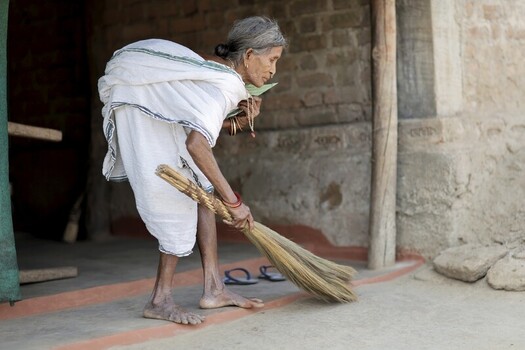 Odisha India 26 March 2026 View of an elderly woman in a white saree gracefully sweeping the ground with a straw broom embodying resilience. Odisha India 26 March 2026 View of an elderly woman in a white saree gracefully sweeping the ground with a straw broom embodying resilience.