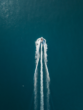 Aerial view of a motorboat cruising through deep blue sea water leaving a long white foam wake in Syracuse Sicily Italy. Aerial view of a motorboat cruising through deep blue sea water leaving a long white foam wake in Syracuse Sicily Italy.