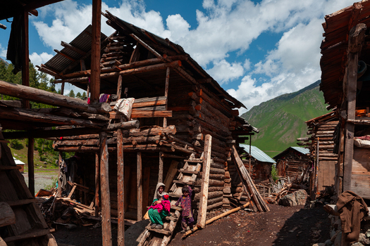 Kail Azad Kashmir Pakistan 01 July 2010 View of a traditional wooden house with a woman and child sitting on the steps in a mountain village surrounded by green hills.