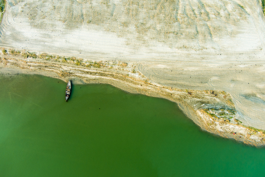Aerial view of a small wooden boat moored along the sandy riverbank of the Padma River with calm green water in Rajshahi Rajshahi Division Bangladesh.