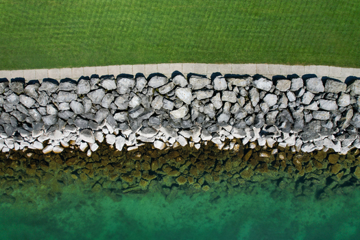 Aerial view of the rocky shoreline of Lake Geneva featuring a stone breakwater a paved walkway and lush green grass Morges Vaud Switzerland. Aerial view of the rocky shoreline of Lake Geneva featuring a stone breakwater a paved walkway and lush green grass Morges Vaud Switzerland.