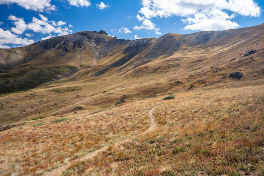 View of the hiking trail leading toward San Luis Peak in the rugged mountain landscape under a bright blue sky with scattered clouds in Creede Colorado United States. View of the hiking trail leading toward San Luis Peak in the rugged mountain landscape under a bright blue sky with scattered clouds in Creede Colorado United States.