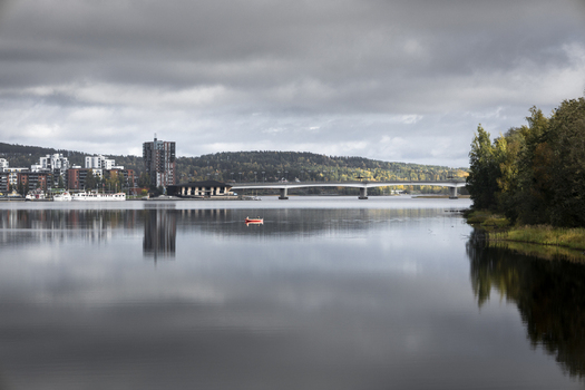 View of the Jyvaskyla cityscape across the calm waters of Lake Jyvasjarvi featuring a bridge buildings and autumn foliage under a cloudy sky in Jyvaskyla Central Finland Finland.