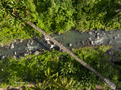 Aerial view of a wooden suspension bridge crossing a rocky river surrounded by lush tropical forest in East Nusa Tenggara Indonesia. Aerial view of a wooden suspension bridge crossing a rocky river surrounded by lush tropical forest in East Nusa Tenggara Indonesia.