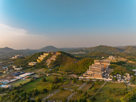 Aerial view of construction sites on green hills with surrounding rural landscape and distant mountains in Udaipur Rajasthan India.