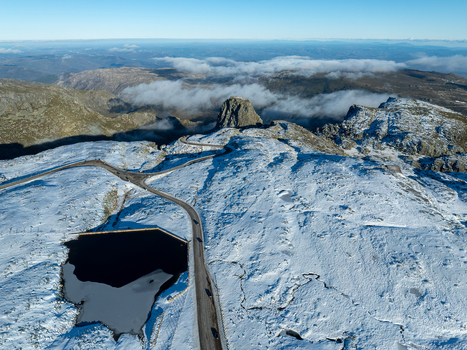 Aerial view of Lago da barragem da Torre in the snow covered Serra da Estrela mountains featuring a winding road and a frozen lake in Manteigas Distrito da Guarda Portugal.