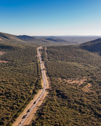 Aerial view of a long road winding through a remote mountain pass in the African wilderness with vehicles travelling between hills and natural bushveld in Lephalale Limpopo South Africa.