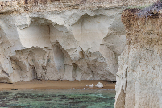 View of white limestone sea caves and a small sandy beach with clear turquoise water Syracuse Sicily Italy.