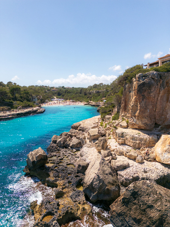 Aerial view of the turquoise waters and rugged limestone cliffs of the Mediterranean coast under a clear blue sky at Cala Llombards Illes Balears Spain. Aerial view of the turquoise waters and rugged limestone cliffs of the Mediterranean coast under a clear blue sky at Cala Llombards Illes Balears Spain.
