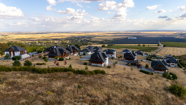 Aerial view of Ruza vetrova resort featuring wooden houses with dark roofs set amidst rolling hills and agricultural fields in Mala Remeta Vojvodina Serbia.