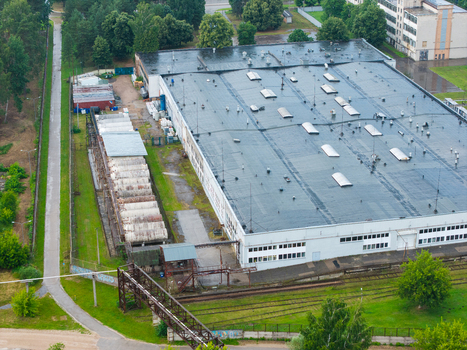 Olaine parish Latvia 04 July 2026 Aerial view of an industrial facility with a large flat roof multiple skylights adjacent railway tracks and surrounding green trees. Olaine parish Latvia 04 July 2026 Aerial view of an industrial facility with a large flat roof multiple skylights adjacent railway tracks and surrounding green trees.