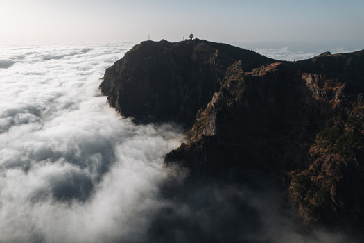 Aerial view of stark dark cliffs rising majestically above a sea of ethereal clouds a dance of light and shadow Pico do Areeiro Madeira Portugal.