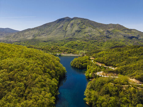 Aerial view of the Blue Eye natural spring in Finiq surrounded by lush green forests winding roads and a mountain range in Finiq Vlore County Albania. Aerial view of the Blue Eye natural spring in Finiq surrounded by lush green forests winding roads and a mountain range in Finiq Vlore County Albania.
