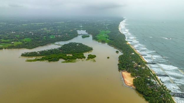 Aerial view of Mattu Beach with lush palm trees green fields and the river meeting the Arabian Sea under a cloudy sky in Udupi Karnataka India.