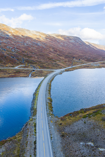 Aerial view of a road crossing a blue lake surrounded by autumn colored mountains in Skjak Innlandet Norway. Aerial view of a road crossing a blue lake surrounded by autumn colored mountains in Skjak Innlandet Norway.