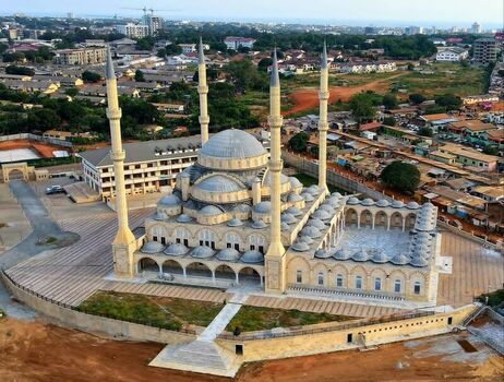 Aerial view of the National Mosque of Ghana with its large central dome and four tall minarets surrounded by urban buildings and paved courtyards in Ghana. Aerial view of the National Mosque of Ghana with its large central dome and four tall minarets surrounded by urban buildings and paved courtyards in Ghana.