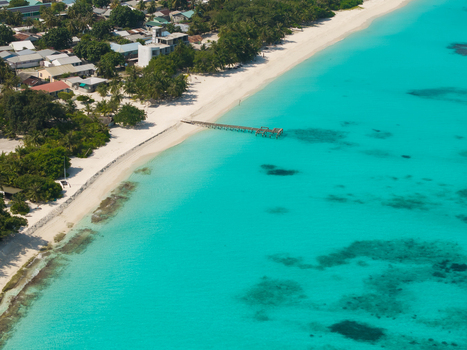 Aerial view of turquoise waters meeting the sandy shore contrasted by the island s lush greenery and structures Vashafaru Island Thiladhummathi Atoll Maldives.