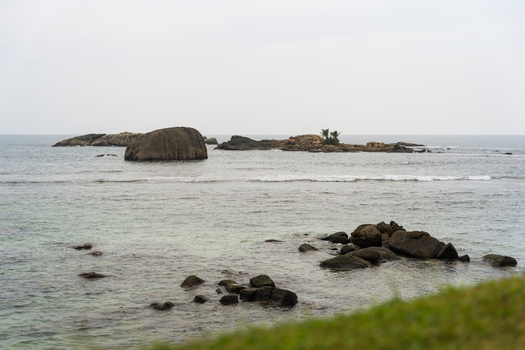 View of large rock formations scattered in the calm turquoise ocean under an overcast sky Galle Southern Province Sri Lanka.