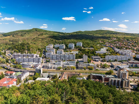 Aerial view of Salgotarjan city center in Hungary showing apartment blocks civic buildings roads and rail lines between forested hills on a clear summer day. Aerial view of Salgotarjan city center in Hungary showing apartment blocks civic buildings roads and rail lines between forested hills on a clear summer day.