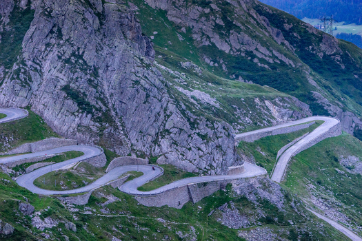 View of the winding Tremola road at Sankt Gotthard Pass with historic stone walls and hairpin turns along the rugged alpine slopes in Airolo Ticino Switzerland.