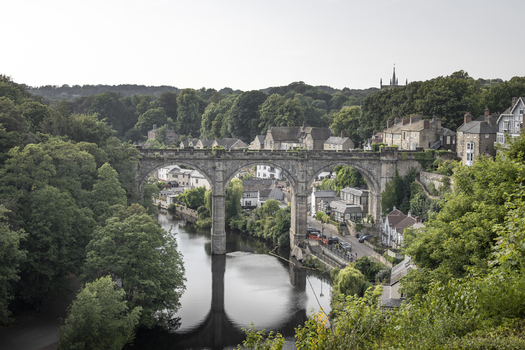 View of the historic Knaresborough Viaduct spanning the River Nidd surrounded by dense green trees and traditional stone buildings in Knaresborough England United Kingdom.