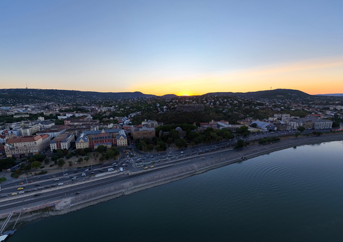 Aerial view of the Danube riverbank and Buda cityscape in Budapest Hungary with tram tracks road traffic and hillside neighborhoods beneath a summer sunset. Aerial view of the Danube riverbank and Buda cityscape in Budapest Hungary with tram tracks road traffic and hillside neighborhoods beneath a summer sunset.