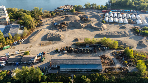 Aerial view of an industrial site featuring large gravel piles storage warehouses and heavy machinery situated along the riverbank in Sremska Mitrovica Vojvodina Serbia.