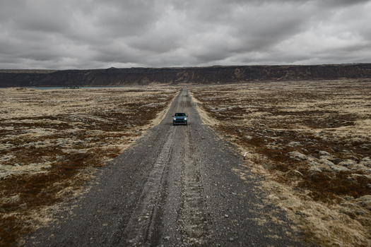 Aerial view of a car driving on a gravel road through the vast mossy landscape of Hlidarvatn in Sveitarfelagid Olfus Iceland. Aerial view of a car driving on a gravel road through the vast mossy landscape of Hlidarvatn in Sveitarfelagid Olfus Iceland.
