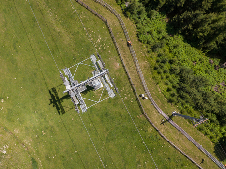 Aerial view of cable car infrastructure and mountain transport system set against lush green alpine meadows and forest in Imst Tyrol Austria.