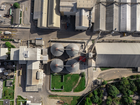 Aerial view of an industrial complex featuring large metal grain silos and warehouses surrounded by paved roads and green areas in Bajos de Haina San Cristobal Provinc Dominican Republic.