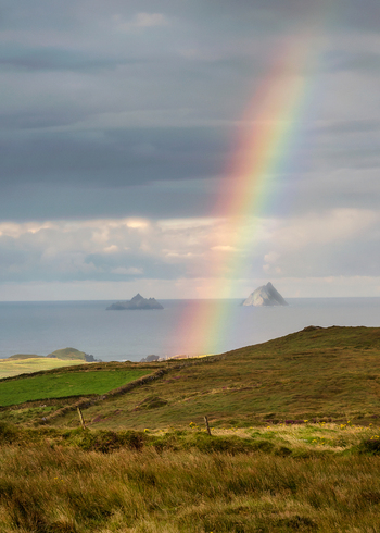 View of a vibrant rainbow stretching across a cloudy sky over the Atlantic Ocean with Great Skellig and Little Skellig islands in the distance County Kerry Ireland. View of a vibrant rainbow stretching across a cloudy sky over the Atlantic Ocean with Great Skellig and Little Skellig islands in the distance County Kerry Ireland.