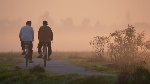 View of two men riding bicycles in misty Bogura Bangladesh.