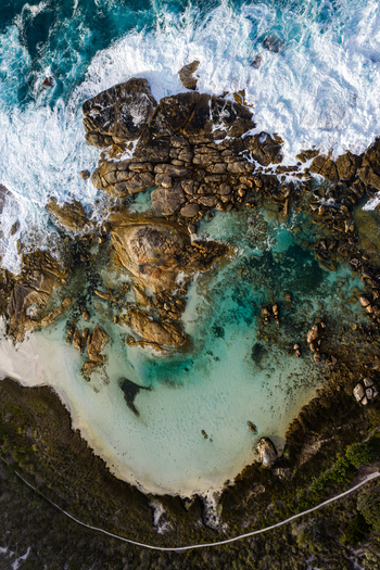 Aerial view of Two Peoples Bay Nature Reserve featuring turquoise waters rugged granite boulders white sand beach and crashing waves in Albany Western Australia Australia.