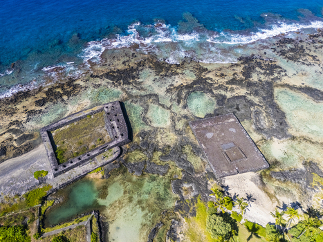 Aerial view of the ancient stone heiau at Kahaluu Beach Park along the rocky volcanic coastline with turquoise waters and palm trees in Kailua Kona Hawaii United States. Aerial view of the ancient stone heiau at Kahaluu Beach Park along the rocky volcanic coastline with turquoise waters and palm trees in Kailua Kona Hawaii United States.