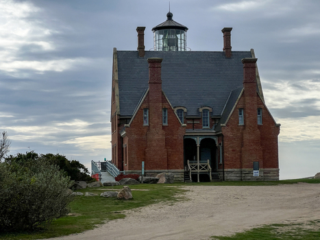 View of the historic Block Island Southeast Light featuring a red brick facade and slate roof under a cloudy sky in New Shoreham Rhode Island United States.