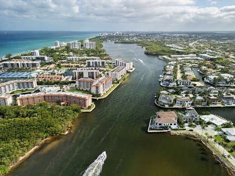 Aerial view of luxury waterfront apartments and residential homes along the Intracoastal Waterway with a boat cruising through the channel Boca Raton Florida United States. Aerial view of luxury waterfront apartments and residential homes along the Intracoastal Waterway with a boat cruising through the channel Boca Raton Florida United States.