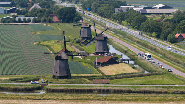 Aerial view of the historic Schermerhorn windmills surrounded by lush green fields canals and a road with passing traffic in Schermerhorn North Holland Netherlands. Aerial view of the historic Schermerhorn windmills surrounded by lush green fields canals and a road with passing traffic in Schermerhorn North Holland Netherlands.