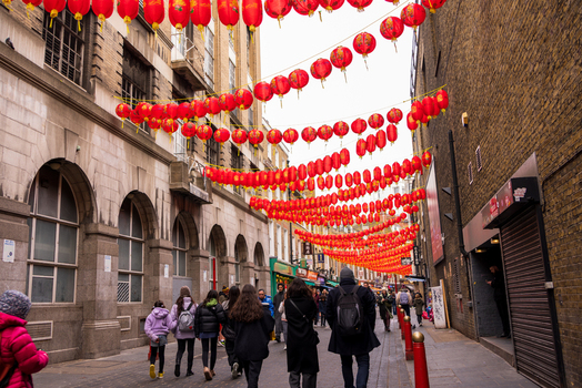 London United Kingdom 12 May 2025 View of the vibrant Chinatown district decorated with rows of red Chinese lanterns hanging above a street filled with people walking past historic brick buildings.