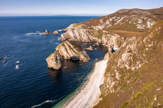 Aerial view of Glenlough Bay featuring rugged cliffs sea stacks and a secluded beach with clear blue water in Ardara County Donegal Ireland.
