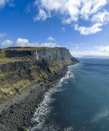 Aerial view of Talisker Bay Beach featuring dramatic cliffs with a waterfall and rocky shoreline under a blue sky Isle of Skye Scotland United Kingdom. Aerial view of Talisker Bay Beach featuring dramatic cliffs with a waterfall and rocky shoreline under a blue sky Isle of Skye Scotland United Kingdom.