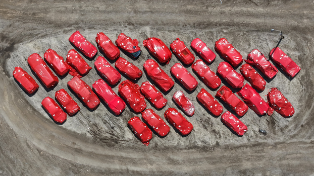 Aerial view of many new cars covered in red protective film parked in a dirt lot in Columbus Ohio United States.