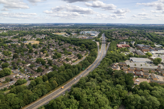 Aerial view of Bretton Park showing a highway cutting through suburban residential areas with lush green trees and buildings in Peterborough England United Kingdom. Aerial view of Bretton Park showing a highway cutting through suburban residential areas with lush green trees and buildings in Peterborough England United Kingdom.